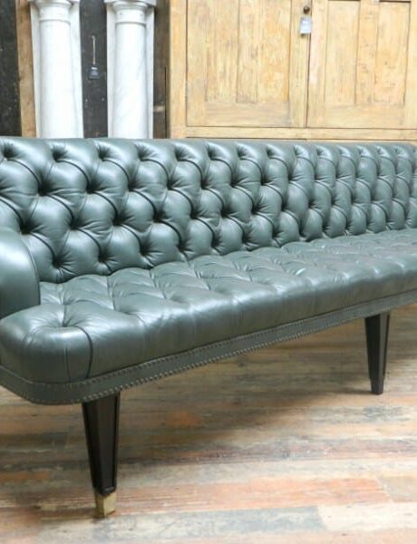 A large deep buttoned green leather sofa on ebonised legs with brass feet.